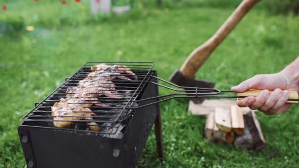 L'uomo gira le ali di pollo arrosto fumante caldo sul barbecue per la buona tostatura, barbecue in cortile nella verde giornata estiva, cucinare all'aperto sul fuoco aperto — Video Stock