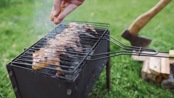 Chef fa barbecue sui carboni caldi della griglia all'aperto e aggiunge spezie alla crosta croccante di ali di pollo, barbecue nel cortile — Video Stock