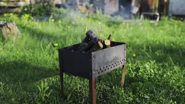 El hombre añade ignición líquida a la pequeña hoguera humeante en la parrilla y se apaga la llama, barbacoa en el patio trasero, haciendo carbones calientes para la cocina en el fuego abierto, barbacoa de verano — Vídeos de Stock