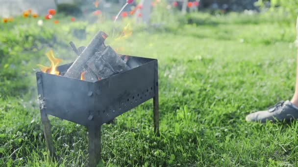 L'uomo aggiunge accensione liquida alla piccola legna fumante nella griglia e scoppia la fiamma, barbecue nel cortile, fare carboni ardenti per la cottura sul fuoco aperto, barbecue estivo — Video Stock