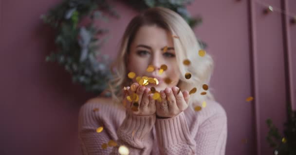 Mooie vrouw in trui blaast glimmende confetti van haar handen naar de camera in slow motion, kerst sfeer, vallende gouden confetti, oudejaarsavond, kerst selebration, 4k Dci 120fps Prores Hq — Stockvideo