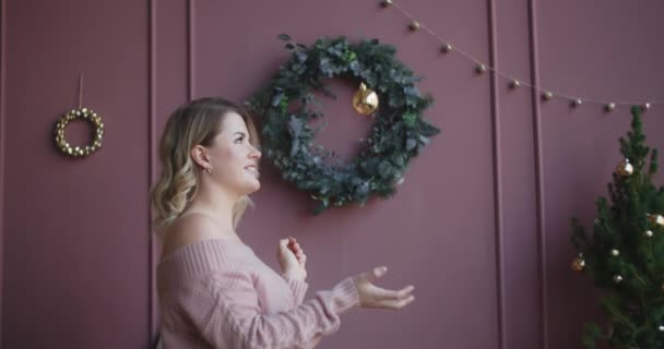 Vonzó nő pulóverben feldob egy karácsonyi labdát lassított felvételen, díszítve a karácsonyfát, hangulatos új évet otthon hangulat, 4k Dci 120fps Prores Hq — Stock videók