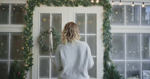 Frau im warmen Pullover wirft schmückt die Haupttüren mit Weihnachtskranz, Dekoration des Weihnachtshauses, gemütliche Atmosphäre im neuen Jahr zu Hause, 4k dci 120fps prores hq — Stockvideo
