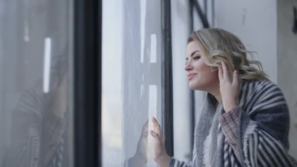 Attractive young woman comes to the big window and looks through it, watching somebody through the glass, checking the weather outdoors, waiting for somebody comming, Full HD 120 fps Prores HQ — Stock Video