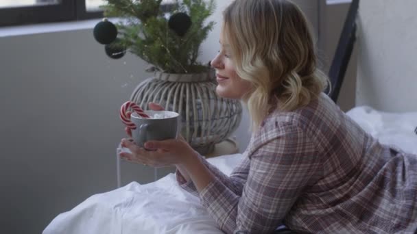 Belle femme en pyjama repose sur le lit et tient une grande tasse de cacao, atmosphère chaleureuse à la maison, chaude soirée d'hiver à la maison, Full HD 120 fps Prores HQ — Video