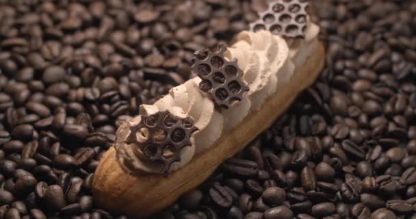 Eclair con crema di caffè e pezzi di cioccolato si trova sui chicchi di caffè nel fascio di luce, dessert in caffè, ripieno per eclairs, pasticceria choux, 4k DCI 120fps Prores 422 HQ 10 bit — Video Stock