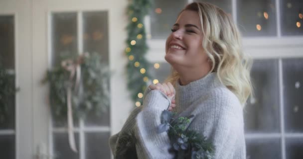 Kobieta w ciepłym swetrze śmieje się ze świątecznego wieńca w dłoniach, zdobiąc skandynawskie wnętrze na święta, przytulna atmosfera nowego roku, 4k Dci 120fps Prores Hq — Wideo stockowe