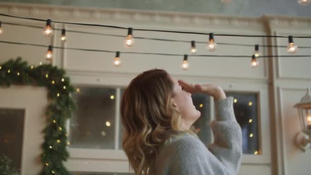 Femme en pull chaud touche guirlandes de lumière sur sa tête, la décoration de l'interrior scandinave pour Noël, atmosphère confortable nouvelle année à la maison, Full HD 120fps Prores HQ — Video