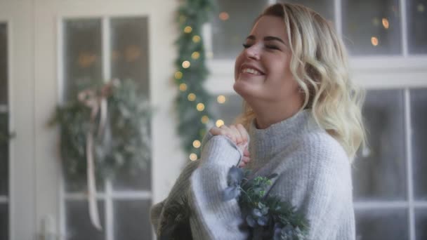 Mujer en suéter cálido se ríe con corona de Navidad en sus manos, la decoración del interior escandinavo para la Navidad, acogedor ambiente nuevo hogar años, Full HD 120fps Prores HQ — Vídeo de stock