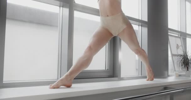 Attraktiv ung blond kvinna sitter på ett garn i slow motion på fönsterbrädan av yoga studio, flexibel kvinna gör akrobatiska och plastiska övningar, yoga och stretching, 4k Dci 60p Prores 422 — Stockvideo