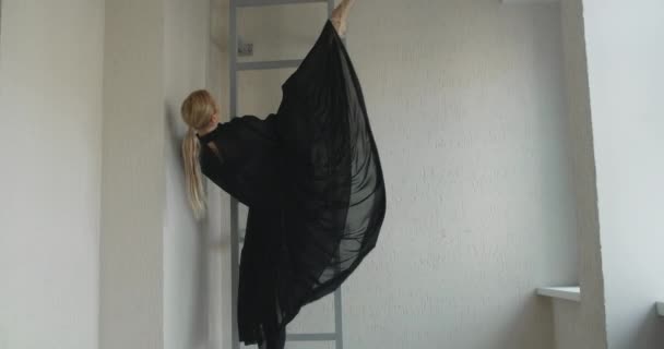 Rubia atractiva bailarina con maquillaje en vestido largo negro hace ejercicios de ballet y trucos en las escaleras, ensayo de ballet, bailarina hace pasos de baile en el traje de escenario, lección de estudio de baile — Vídeo de stock