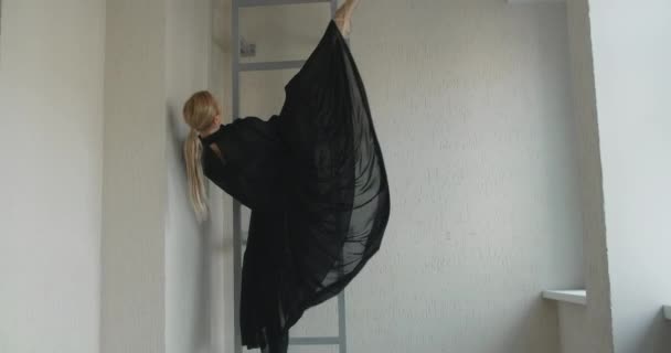 Блондинка привлекательная танцовщица с макияжем в длинном черном платье делает балетные упражнения и трюки на лестнице, балетная репетиция, балерина делает танцевальные шаги в сценическом костюме, урок танцевальной студии — стоковое видео