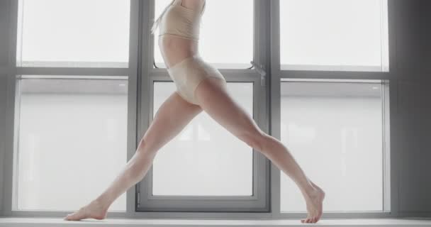 Attraktiv ung blond kvinna sitter på ett garn i slow motion på fönsterbrädan av yoga studio, flexibel kvinna gör akrobatiska och plastiska övningar, yoga och stretching, 4k Dci 60p Prores 422 — Stockvideo