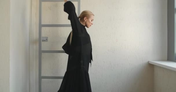 Rubia atractiva bailarina con maquillaje en vestido largo negro hace ejercicios de ballet y trucos en las escaleras, ensayo de ballet, bailarina hace pasos de baile en el traje de escenario, lección de estudio de baile — Vídeo de stock