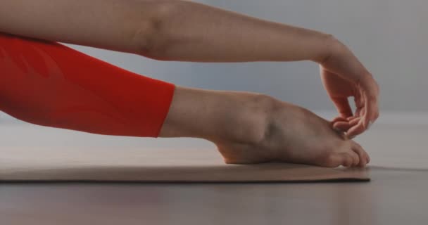 Attraktiv ung kvinna sträcker sig genom att böja sig framåt i sittande ställning på golvet på youga mattan, yoga klasser i slow motion, person gör fysiska övningar, stretching och gymnastik — Stockvideo