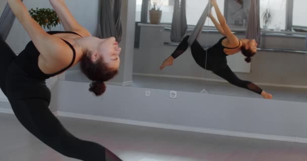 Attraktiv ung kvinna sitter på ett garn i fly yoga hängmatta i slow motion, flexibel kvinna gör akrobatiska och plastiska övningar, yoga och stretching, 4k DCI 60p Prores 422 — Stockvideo