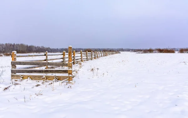 Schneebedecktes Feld auf dem Land. ein hölzerner Zaun aus Ackerland — Stockfoto