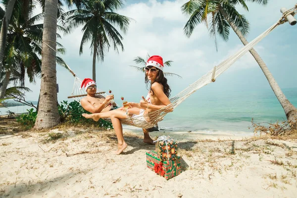 Couple sitting on hammock in Santa hats — Stock Photo, Image