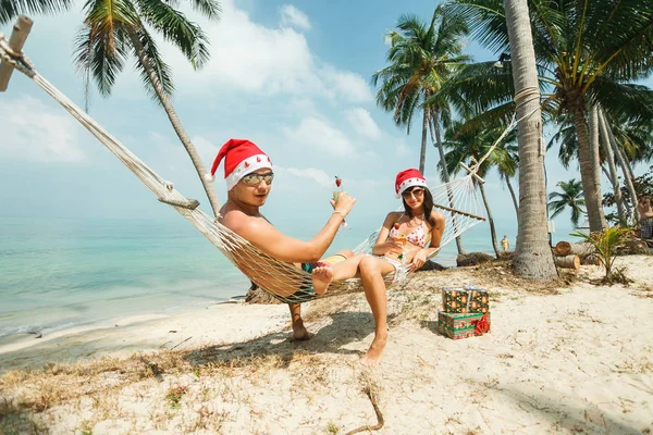 Pareja sentada en hamaca en Santa sombreros —  Fotos de Stock