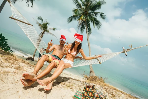 Couple sitting on hammock in Santa hats — Stock Photo, Image