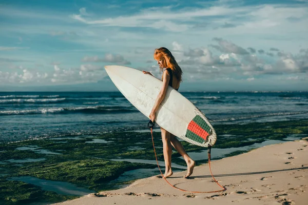 Surfer girl walking with board on the sandy beach. Surfer girl. Beautiful young woman at the beach. water sports. Healthy Active Lifestyle. Surfing. Summer Vacation. Extreme Sport. Bali