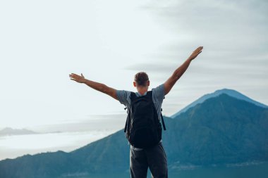 Genç yakışıklı adam eli kazanan yanardağ, güneşli sonbahar sabah üzerinde. Havada kaldırdı elleriyle mutlu hiker rock çam ormanı üzerinde durmak. Sun Vadisi'ne puslu ve sisli sabah üzerinde göster.