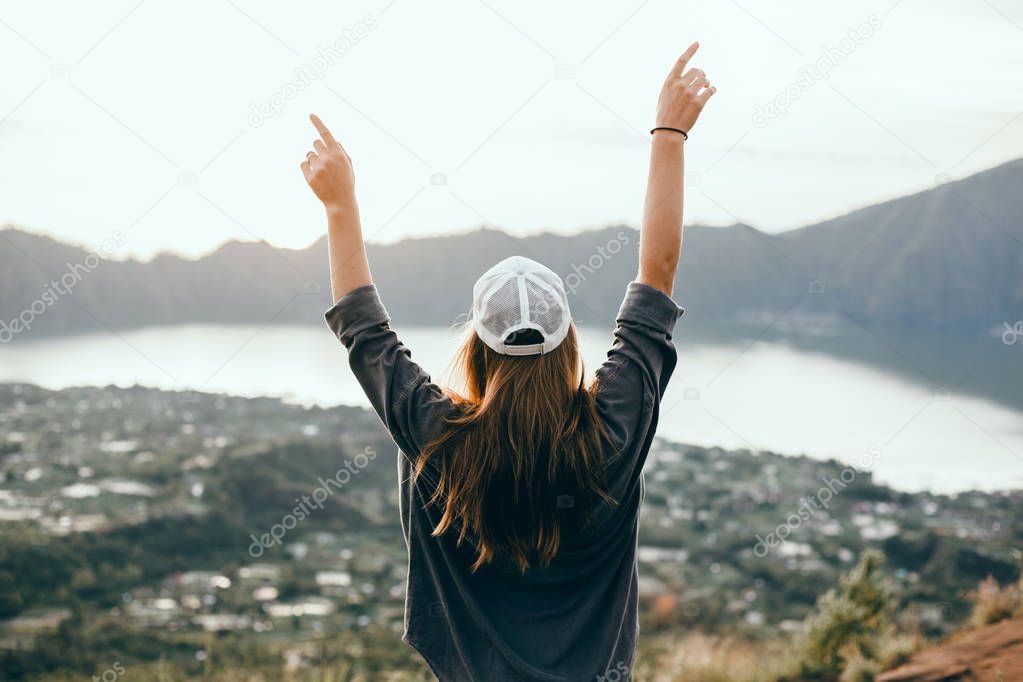 Woman traveler looking at volcano Rinjani, island Lombok. Indonesia.Young backpacker traveling along mountains, happy female walking discovering world, summer vacation concept, hand up winner, Bali