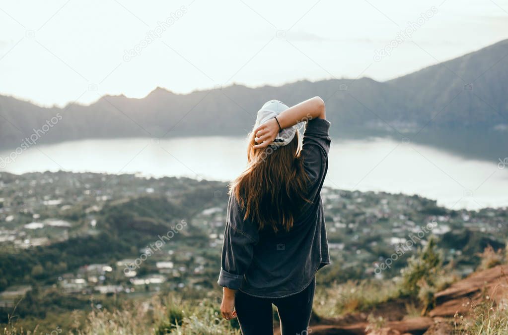 Woman traveler looking at volcano Rinjani, island Lombok. Indonesia.Young backpacker traveling along mountains, happy female walking discovering world, summer vacation concept, hand up winner, Bali