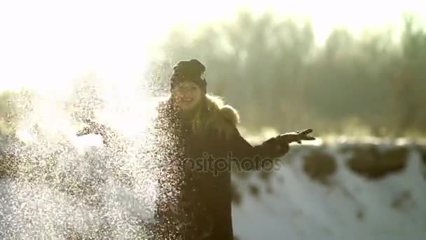 Meisje werpt sneeuw. Gefotografeerd in direct zonlicht. Men ziet een korrel van sneeuw fladderen rond. — Stockvideo