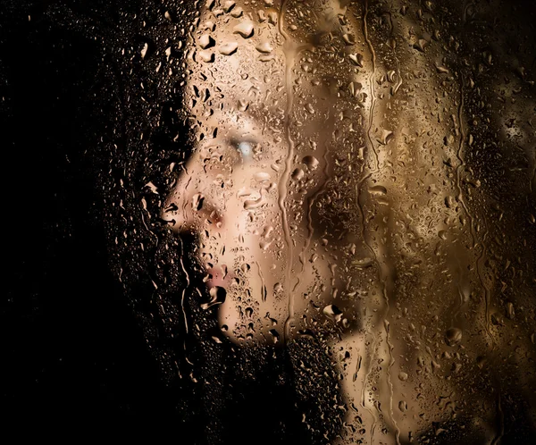 Smooth portrait of sexy model, posing behind transparent glass covered by water drops. young melancholy and sad woman portrait — Stock Photo, Image