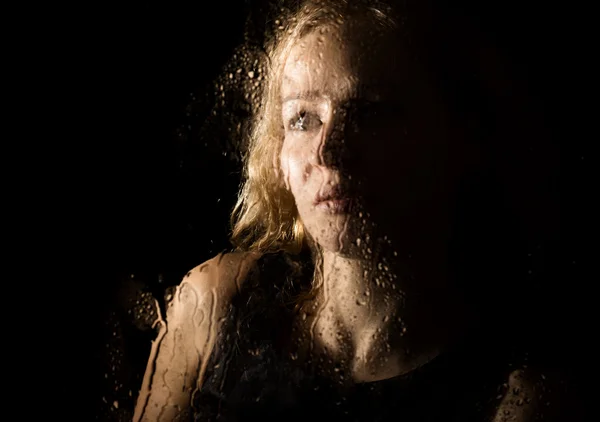 Smooth portrait of sexy model, posing behind transparent glass covered by water drops. young melancholy and sad woman portrait — Stock fotografie