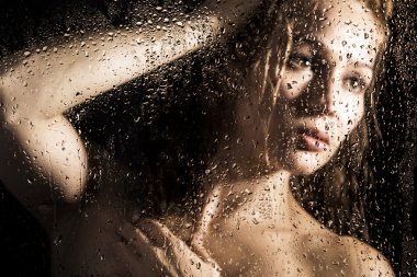 seksi genç kadın, su damlaları ile kaplı şeffaf cam arkasında poz. melankoli ve hüzünlü kadın portresi