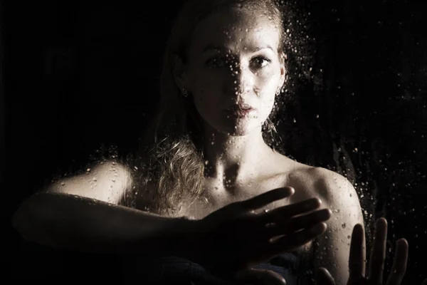 Seksi genç kadın, su damlaları ile kaplı şeffaf cam arkasında poz. melankoli ve hüzünlü kadın portresi — Stok fotoğraf
