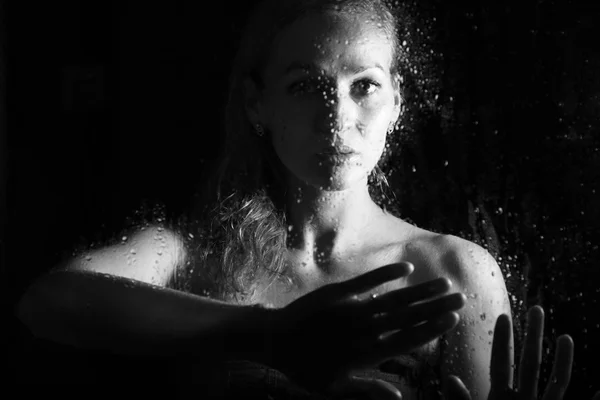 Sexy giovane donna, posa dietro vetro trasparente coperto da gocce d'acqua. ritratto femminile malinconico e triste — Foto Stock