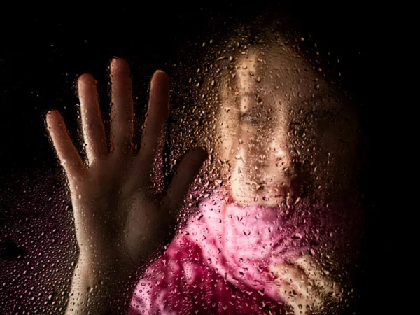Joven mujer triste retrato detrás de la ventana en la lluvia con gotas de lluvia sobre ella —  Fotos de Stock