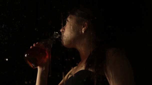 Молодая грустная женщина за окном с капельками на нем. одинокая девушка пьет бренди из бутылки и плачет — стоковое видео