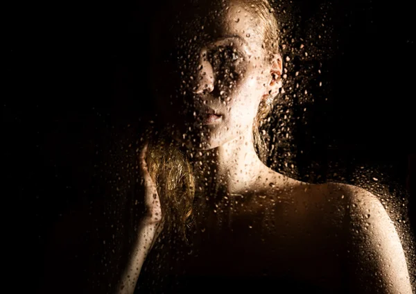 Sexy joven, posando detrás de vidrio transparente cubierto por gotas de agua. retrato femenino melancólico y triste — Foto de Stock