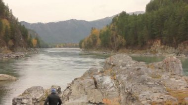 çam ağaçları ile kayalar arasında akan dağ nehri. nehir kıyısında ki büyük bir kayanın üzerinde duran gezgin