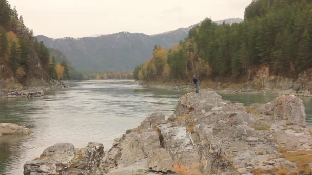 Rivière de montagne qui coule entre des rochers avec des pins. voyageur debout sur un gros rocher au bord de la rivière — Video