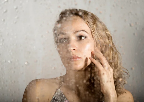 Sexy young woman, posing behind transparent glass covered by water drops. melancholy and sad female portrait — Stock Photo, Image