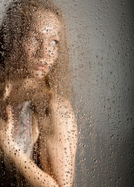 Sexy mladá žena, pózuje za průsvitným sklem pokrytých kapky vody. melancholická a smutná ženská portrét — Stock fotografie