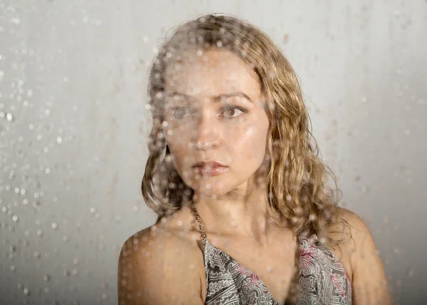 性感的年轻女子，在透明玻璃后面摆姿势，被水滴覆盖。忧郁和悲伤的女性肖像 — 图库照片