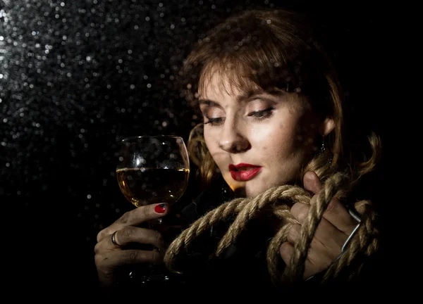 Загадочная молодая женщина с бокалом вина, позирующим за прозрачным стеклом, покрытым водяными капельками. на темном фоне — стоковое фото