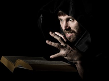 karanlık bir arka plan üzerinde mum ışığında kalın antik kitaptan büyü büyücü çevirir