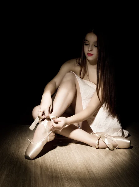 Piękna młoda kobieta Ballerina wiązająca Pointe buty na ciemnym tle — Zdjęcie stockowe