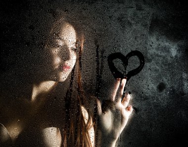 Seksi modelpürüzsüz portre, su damlaları ile kaplı şeffaf cam arkasında poz ve cam bir kalp çizer