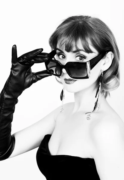 Красотка-ретро женская модель с профессиональным макияжем в длинных кожаных перчатках, держащая сверх размера солнцезащитные очки. черный и белый — стоковое фото