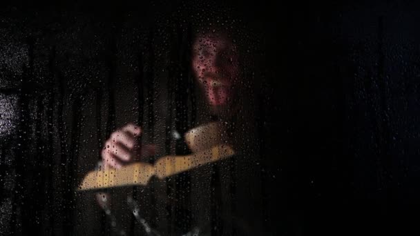 Necromancer casts spells from thick ancient book by candlelight, behind transparent glass covered by water drops on a dark background — Stock video