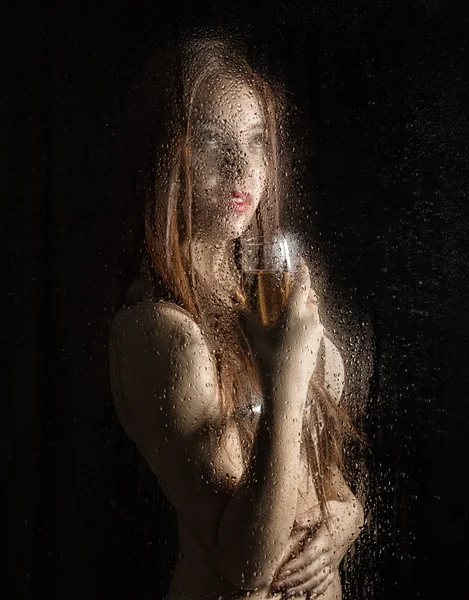 Smooth portrait of sexy model, posing behind transparent glass covered by water drops. young woman holding a glass of champagne — ストック写真