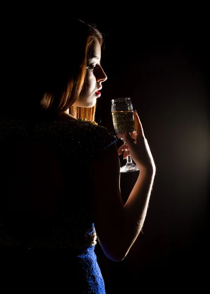 Jovem celebrando mulher em um vestido azul segurando uma taça de champanhe em um fundo escuro. jogo de luz e shedow — Fotografia de Stock